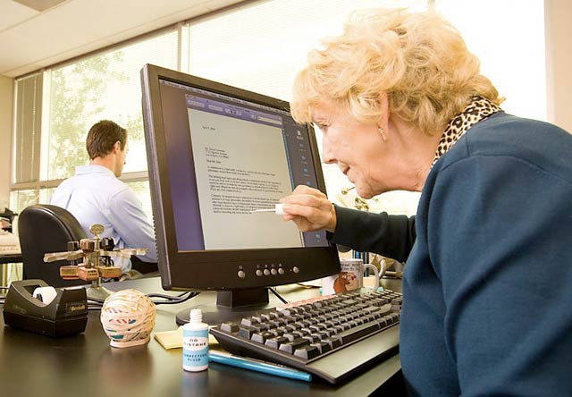 Funny photo of an older woman painting white-out on a computer screen.