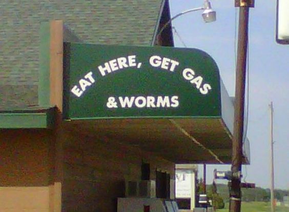 Awning in front of building says, eat here, get gas & worms, a funny cartoon